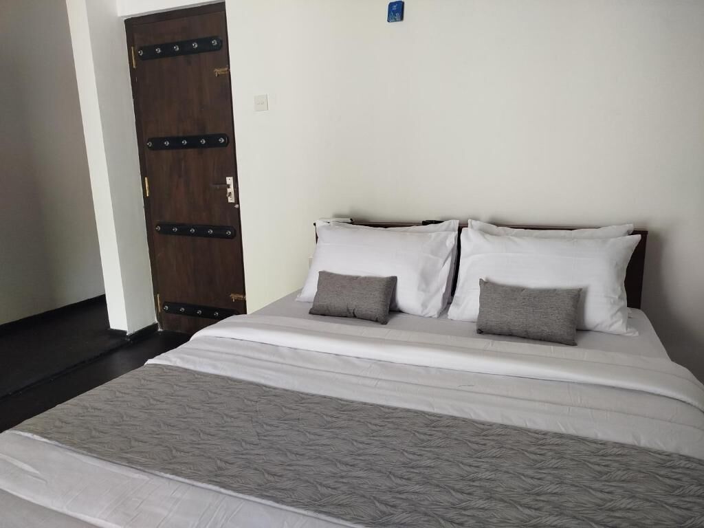 A bed with white bedding and two pillows, a wooden door with metal hardware, and a plain wall.