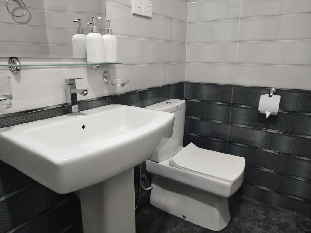 Un baño con lavamanos blanco, inodoro y repisa de vidrio con artículos de aseo.