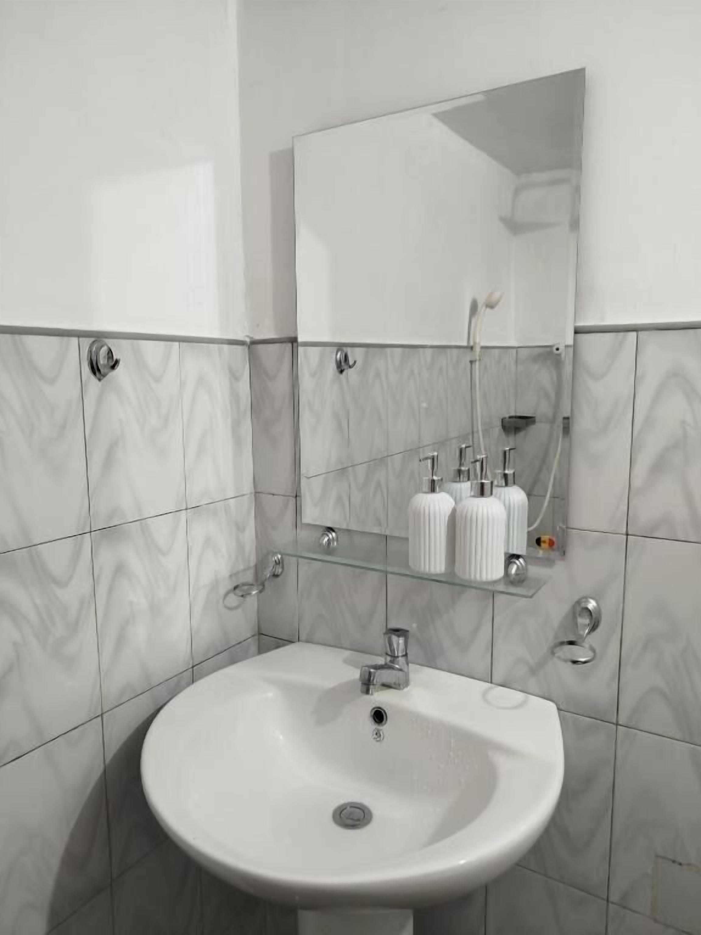 A bathroom with a white sink, a mirror, and a glass shelf with toiletries.