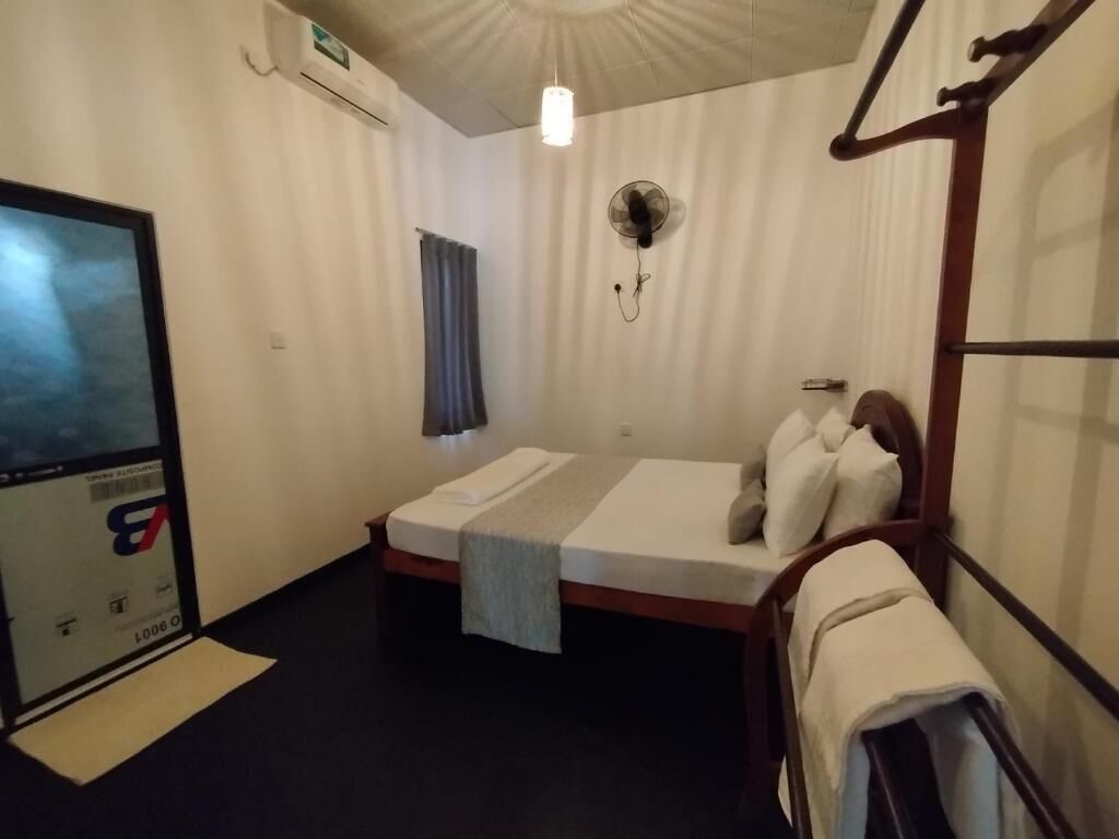 A room with a bed, a fan, a window with curtains, and an air conditioning unit.