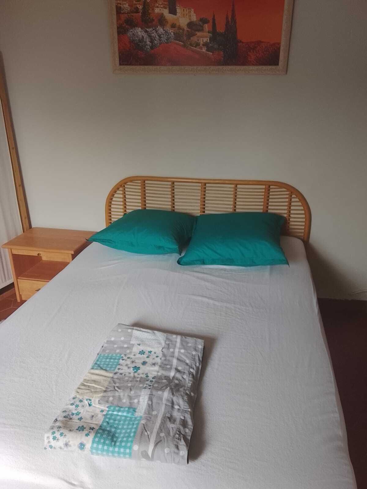 Una cama con sábana blanca, dos almohadas color turquesa y una manta doblada con estampado floral.