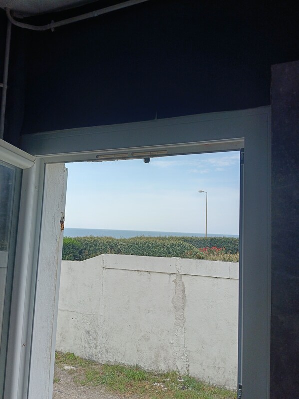 An open door leading to a balcony with a view of a distant landscape, a concrete wall, and a streetlight.