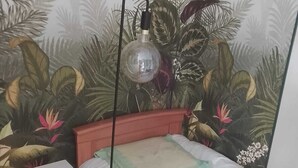 Un dormitorio con una cama, un taburete pequeño blanco, una lámpara de pie y un mural temático de la selva tropical.
