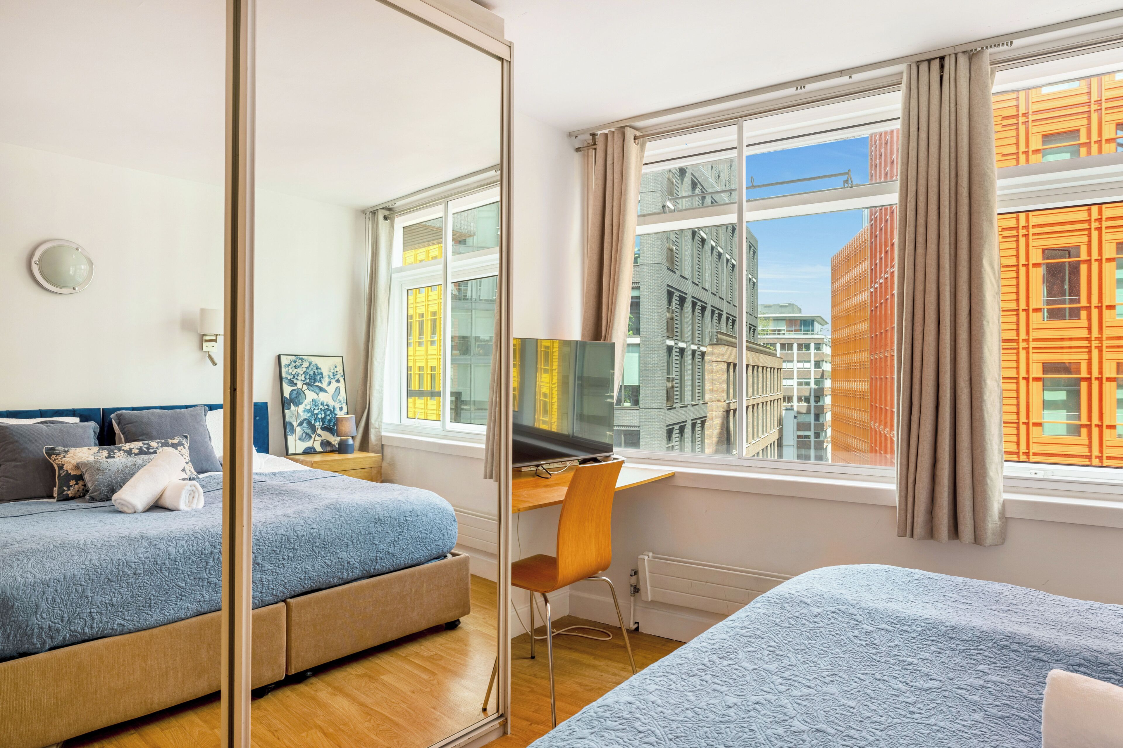 Een hotelkamer met een bed, een bureau, een stoel, een spiegel en een raam met uitzicht op de stad.
