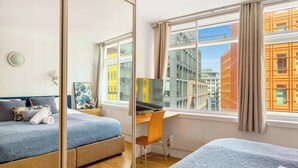 Et hotelværelse med seng, skrivebord, stol, spejl og et vindue med udsigt over byen.