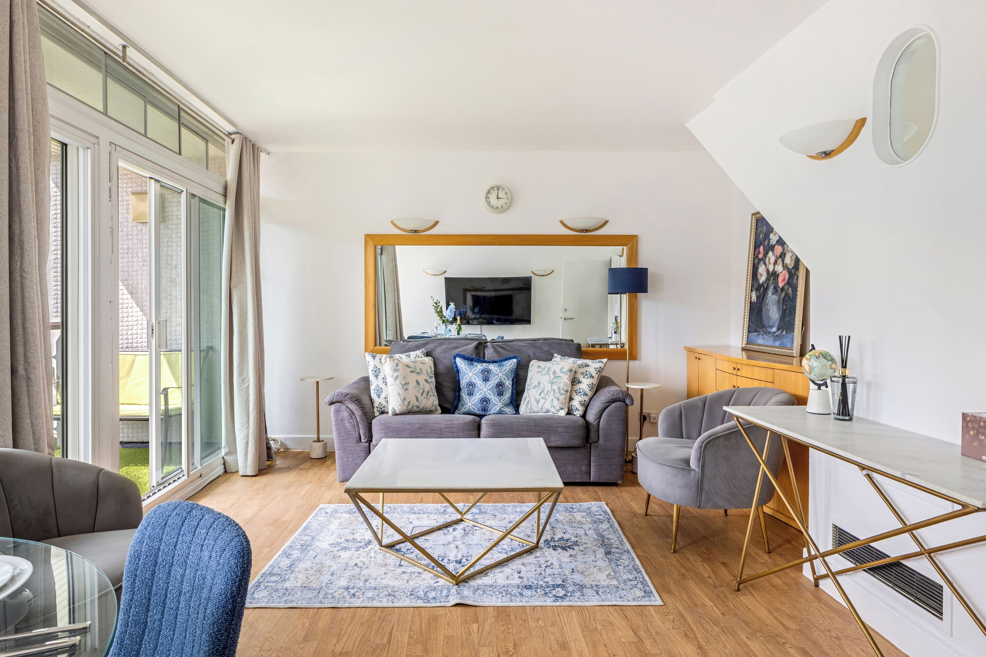 Een moderne woonkamer met een grijze bank, een salontafel, en een eethoek met een witte tafel en stoelen.