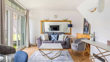 Een moderne woonkamer met een grijze bank, een salontafel, en een eethoek met een witte tafel en stoelen.