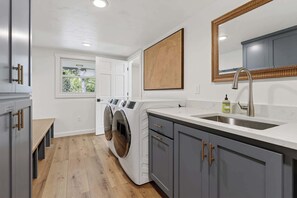 A laundry room with a washing machine, a sink, and cabinets.