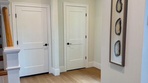 Un corridoio con pavimento in legno, porte bianche e un quadro appeso al muro.