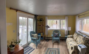 A cozy living room with a sofa, two chairs, a bookshelf, and a view of a deck.