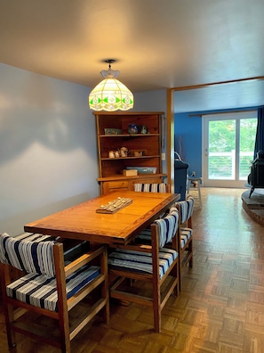 A dining area with a wooden table and striped cushioned benches, a wooden bookshelf, and a hanging light fixture.