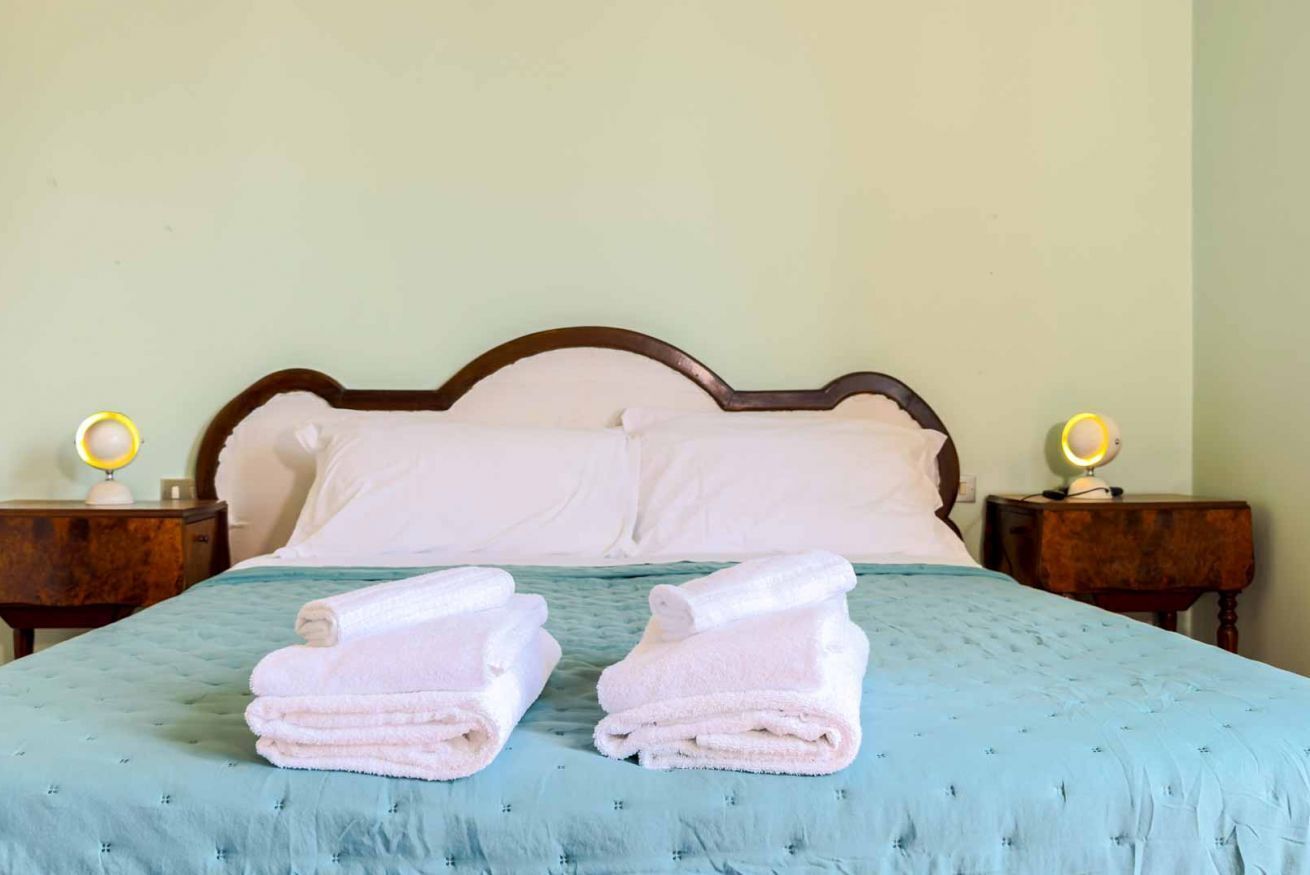 Uma cama com cobertura azul acolchoada, duas almofadas brancas e duas toalhas dobradas sobre a cama.