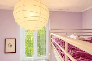 Una habitación con una cama nido, una lámpara colgante, una ventana con vistas a la vegetación y un cuadro en la pared.