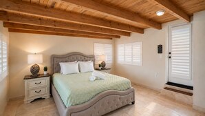 Ein Schlafzimmer mit Bett, Nachttischen, einer Lampe, einem Blumentopf und einer Tür mit Fenster.