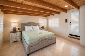 A bedroom with a bed, nightstands, a lamp, a potted plant, and a door with a window. - Amazing Location! Steps To Sand, Ocean/Sunset View (Oxnard)