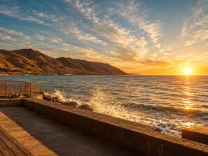 A coastal scene with a sunset, waves crashing against a concrete barrier, and mountains in the background. - 25% Off Sept 18&19! Water Front Perfect 4 Families (Ventura)