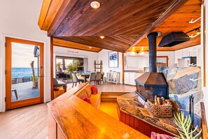 A cozy interior with a wooden ceiling, a stone fireplace, and a view of the ocean through a glass door. - Oceanfront Retreat, Amazing Ocean Views W/Jacuzzi! (Ventura)