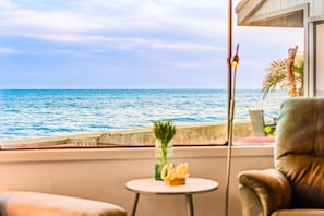 A room with a view of the sea, a small table with a vase, and a chair.