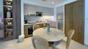 A modern kitchen with a dining table, chairs, a microwave, and a refrigerator. - Stylish Studio Apartment with Kitchen, TV Lounge & Dining Space (Muḥāfaẓat al-Muḥarraq)