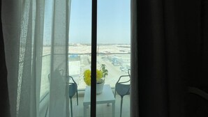 A balcony with a view of a parking lot and buildings, a table with chairs, and a potted plant. - Stylish Studio Apartment with Kitchen, TV Lounge & Dining Space (Muḥāfaẓat al-Muḥarraq)