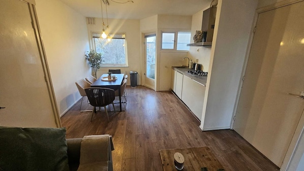 A compact kitchen with a dining area, wooden flooring, and a view through the window.