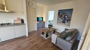 A compact living space with a kitchenette, a sofa, a coffee table, a television, and a poster on the wall.