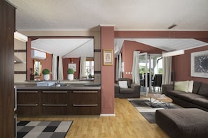 Eine moderne Küche mit Kochinsel, ein Essbereich mit Sofa und Sesseln sowie ein Wohnzimmer mit Couch und Couchtisch.