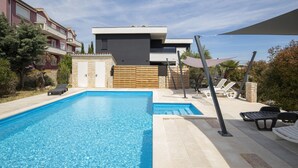 A modern pool area with a rectangular pool, lounge chairs, and a stone wall. - Apartment Valentino 5 with shared Pool (Ližnjan)