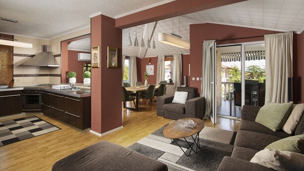A modern kitchen with dark cabinetry, a dining area with a table and chairs, a living room with a sofa and a coffee table, and a sliding glass door leading to an outdoor patio. - Apartment Valentino 5 with shared Pool (Ližnjan)