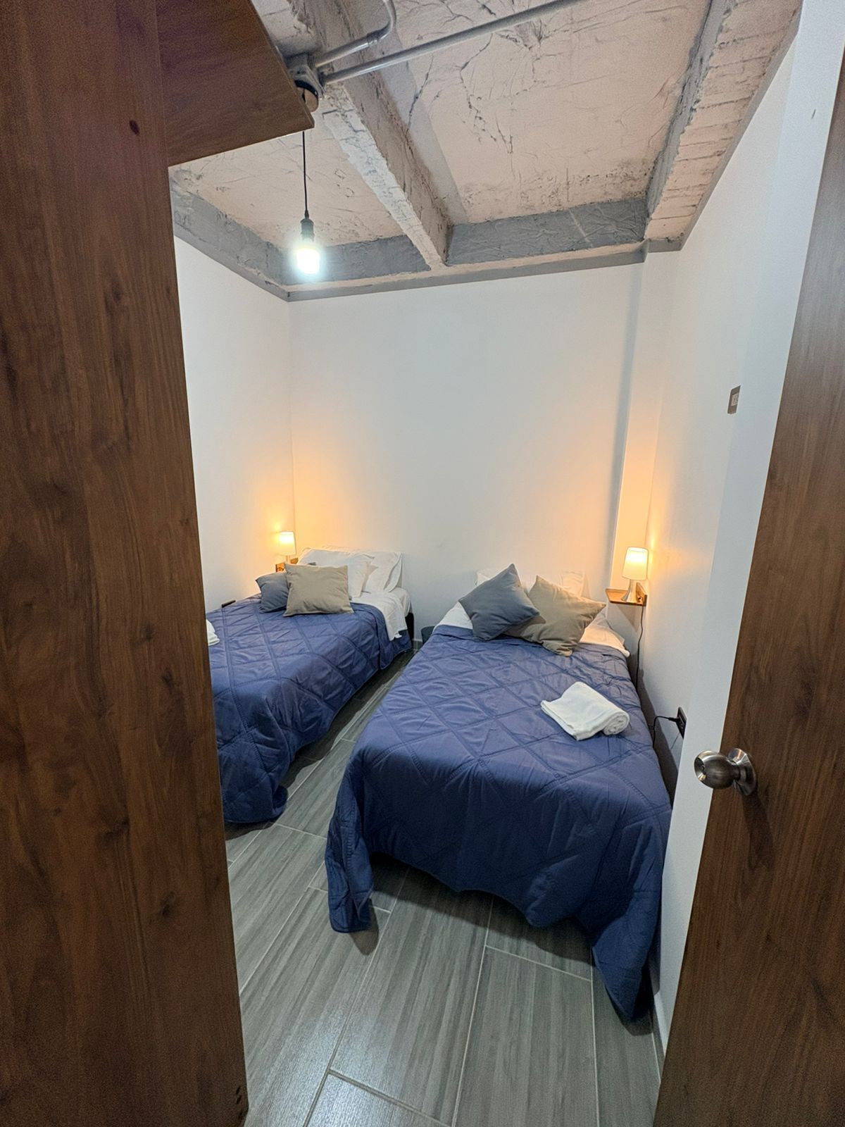 Una habitación con dos camas, cada una con cabecera, una puerta de madera y techo con vigas a la vista.