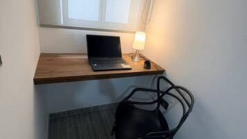 A small workspace with a laptop on a wooden shelf, a desk lamp, and a black chair.