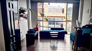 A room with a sofa, a coffee table, a potted plant, and a view of buildings outside. - GUADUAS, CLOSE TO THE HISTORICAL CENTER, PET FRIENDLY, APARTMENT2H+2B,WIFI -PARKING (Guaduas)