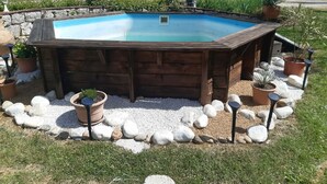 Ein hölzernes Whirlpoolbad, umgeben von Steinen und Blumentöpfen.