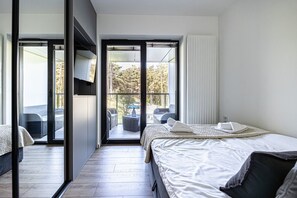 Ein modernes Hotelzimmer mit einem großen Bett, einem Balkon mit Sitzgelegenheit und Blick auf Bäume und ein Auto.