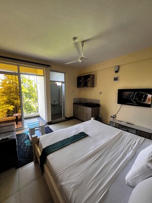 Una camera d'albergo con un letto, una TV, il bagno e un balcone vista alberi.