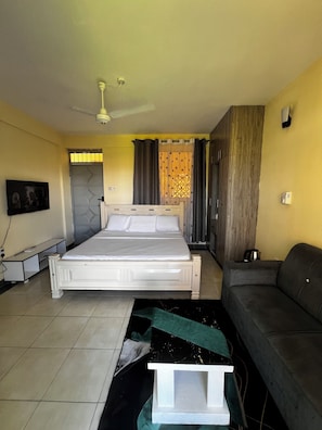 A bedroom with a bed, a ceiling fan, a grey sofa, a TV, and a window with curtains. - Chic Studio In Mtwapa(Cozy-Serena environment) (Mtwapa)