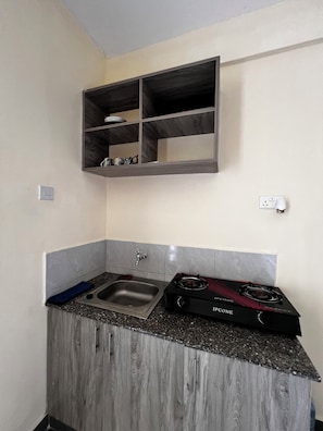 A compact kitchen with a built-in gas stove, a sink, and a shelf above the counter. - Chic Studio In Mtwapa(Cozy-Serena environment) (Mtwapa)