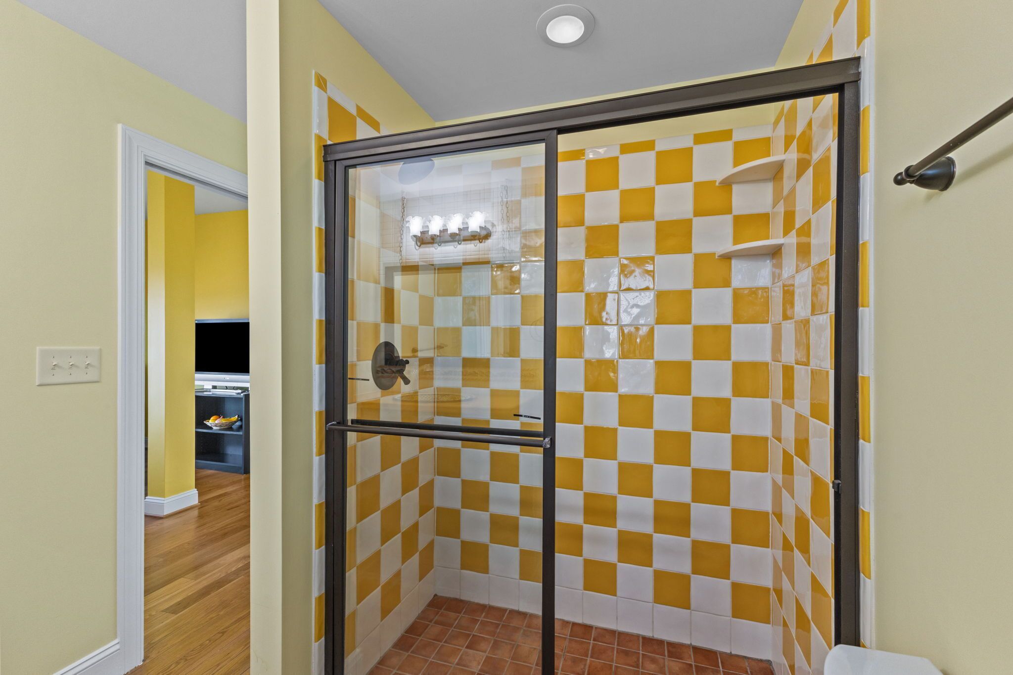 A bathroom with yellow and white checkered tiles, a glass shower enclosure, and a visible toilet.