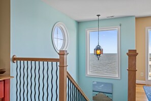 A staircase with a wooden handrail and a wavy metal railing, a hanging lantern, and a framed picture of the sea. - Water Wonderland - Panoramic Water Views, Dockage Available, Core Sound (Sea Level)