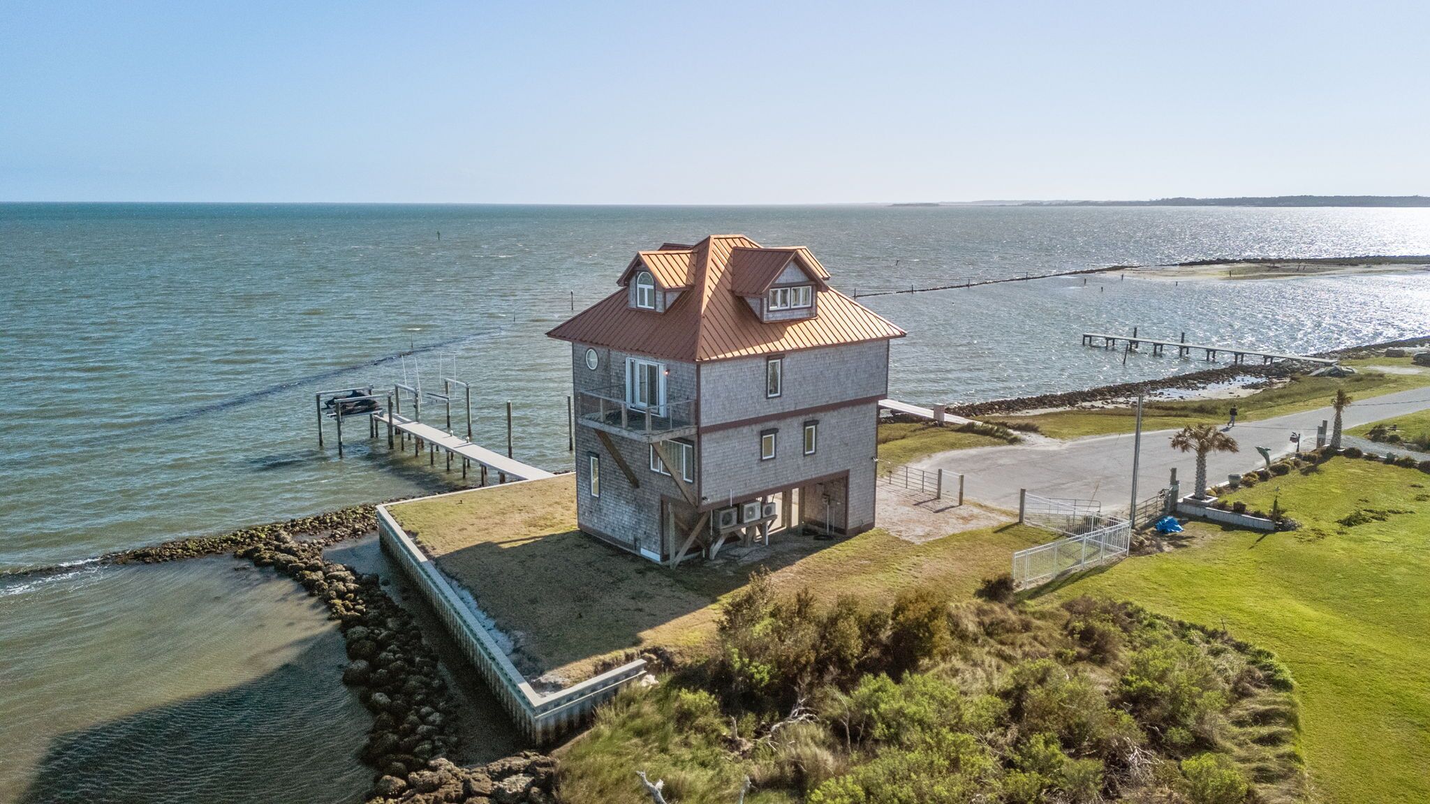 A two-story building with a red roof, a dock, and a view of the sea.