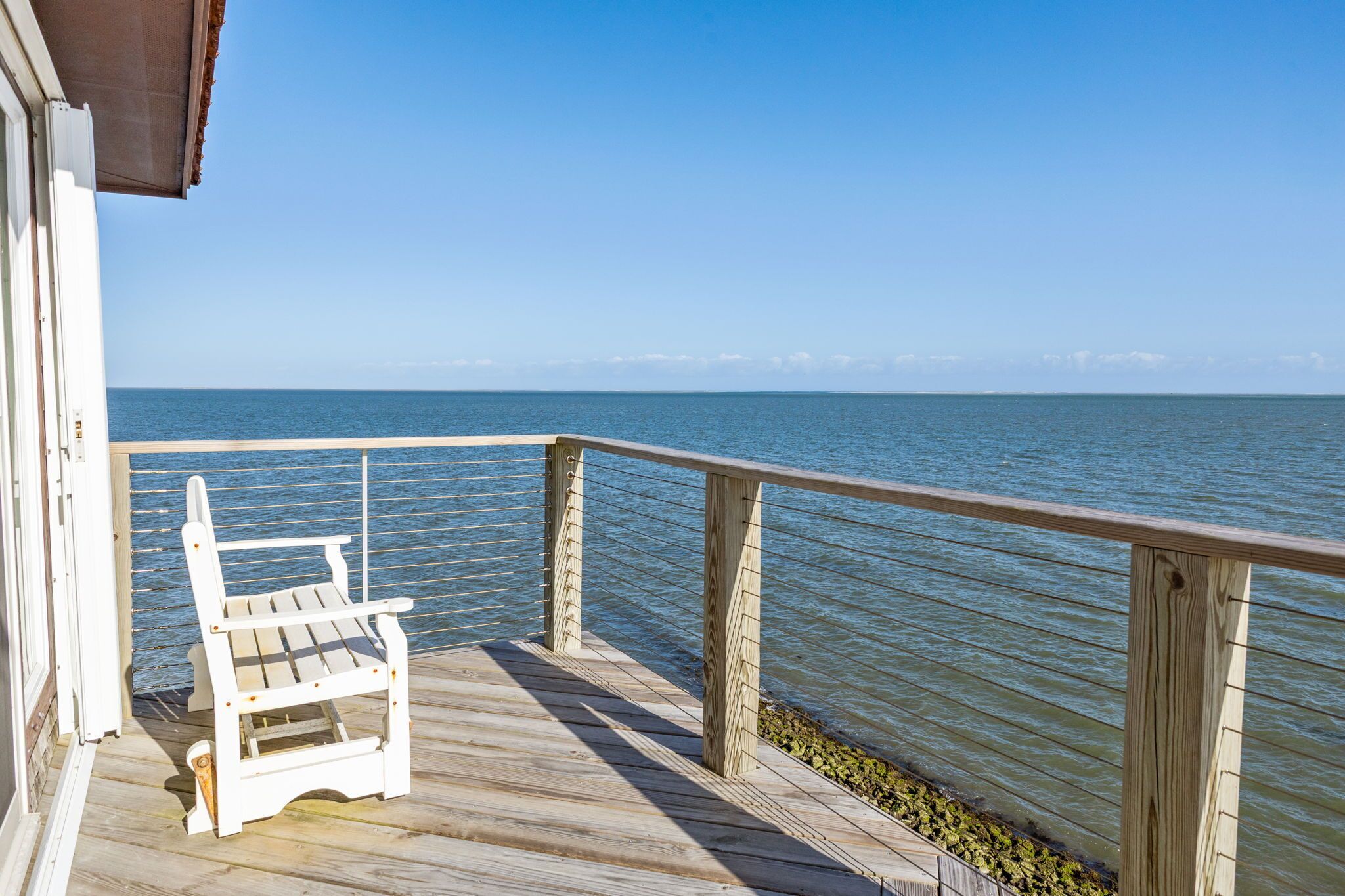 Een houten terras met een witte stoel, uitkijkend op een rustig wateroppervlak.