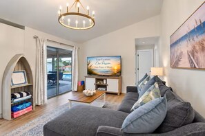 Uma sala de estar moderna com um sofá cinzento, uma televisão de tela plana e um lustre.