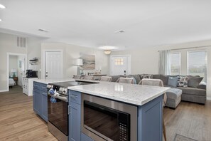 Eine moderne Küche mit Einbauofen und Mikrowelle, ein Essbereich mit Tisch und Stühlen sowie ein Wohnzimmer mit Sofa und Couchtisch.
