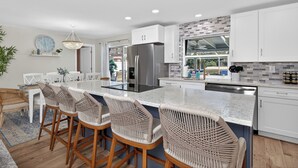 Una cocina moderna con armarios blancos, un refrigerador de acero inoxidable y una zona de bar con sillas de mimbre.
