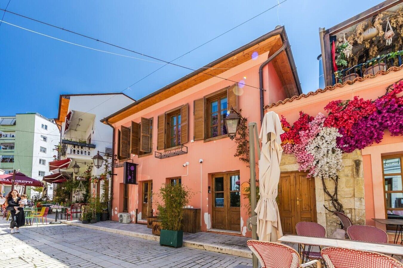 A street with a pink building, outdoor seating, and a clear sky.