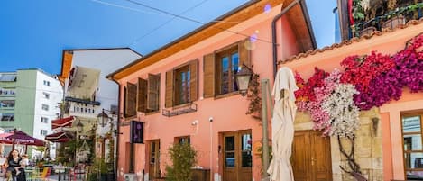 A street with a pink building, outdoor seating, and a clear sky.