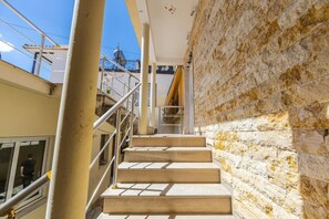Eine Treppe, die zu einer oberen Ebene führt, mit einer Steinwand auf der einen Seite und einem Metallgeländer auf der anderen.