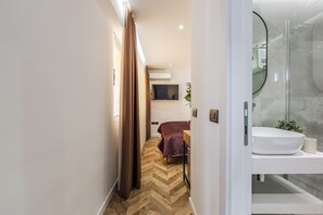 Een moderne hotelkamer met een visgraatvloer, een bed met bruine spreidek en een aan de muur bevestigde televisie, plus een douchecabine van glas.