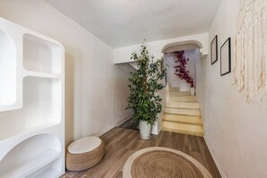 Ein Flur mit Treppe, weißen Wänden, einer großen Topfpflanze und einem strukturierten Wandkunstwerk.