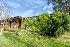 A modern house with a brick facade, a covered porch, and a well-maintained garden with various plants and a small tree. - The Keelendi House | Hunter Valley Spa Retreat (Bellbird Heights)
